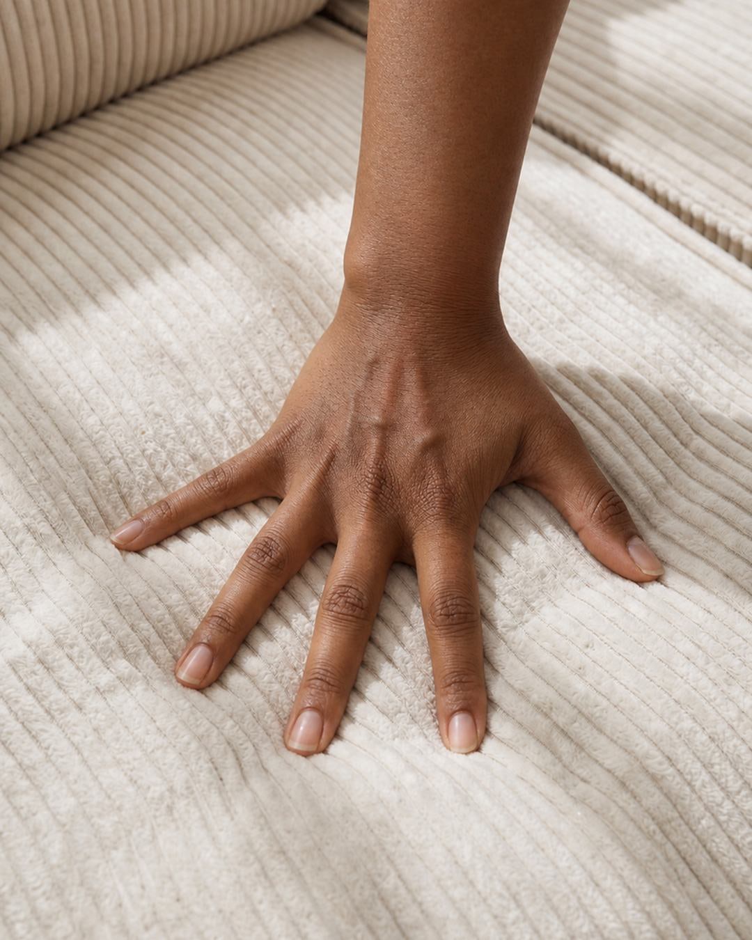 A hand pressing into ribbed cream corduroy, the foam giving deeply beneath it.