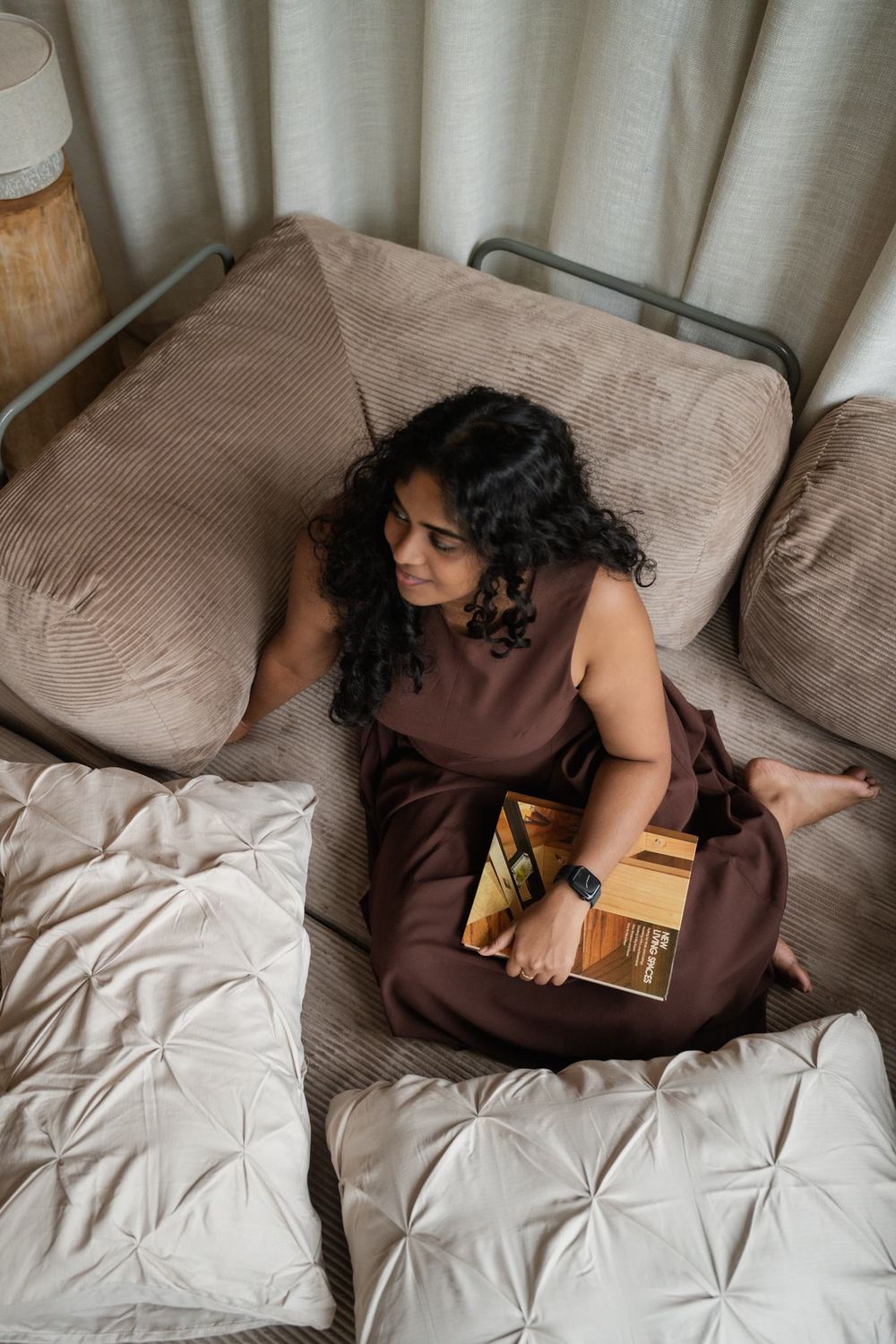 A woman sitting cross-legged on the taupe corduroy Cloud Lounge, reading a book on interiors.