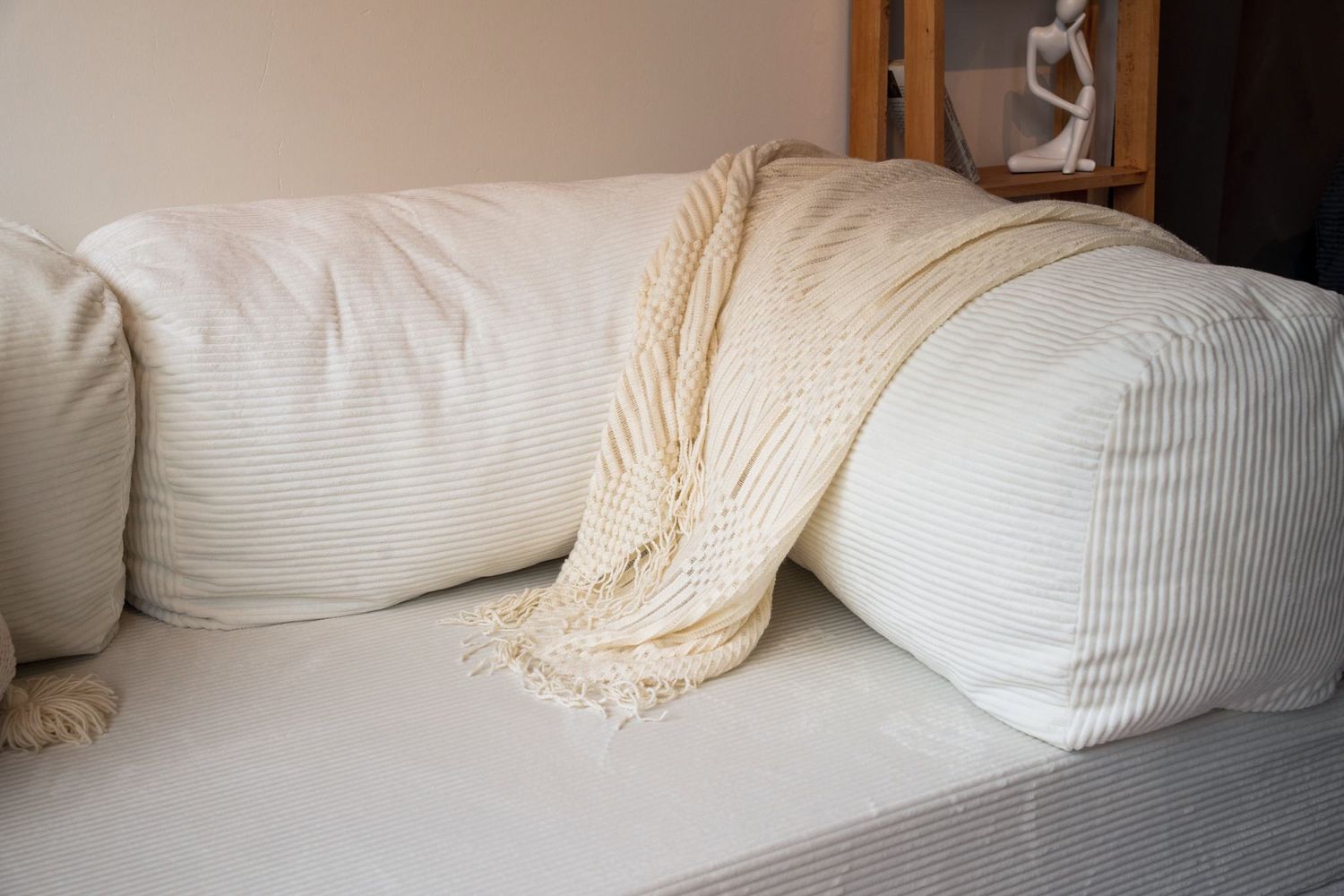 The Cloud Sofa in cloud white corduroy, a fringed throw draped across the backrest.